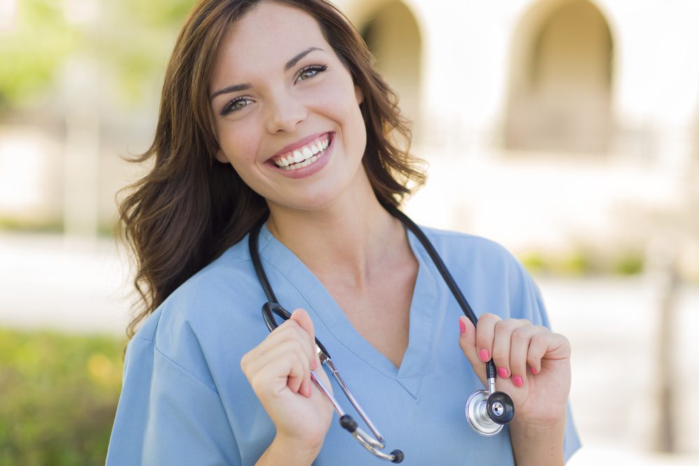 Woman in scrubs smiling holding a stethoscope