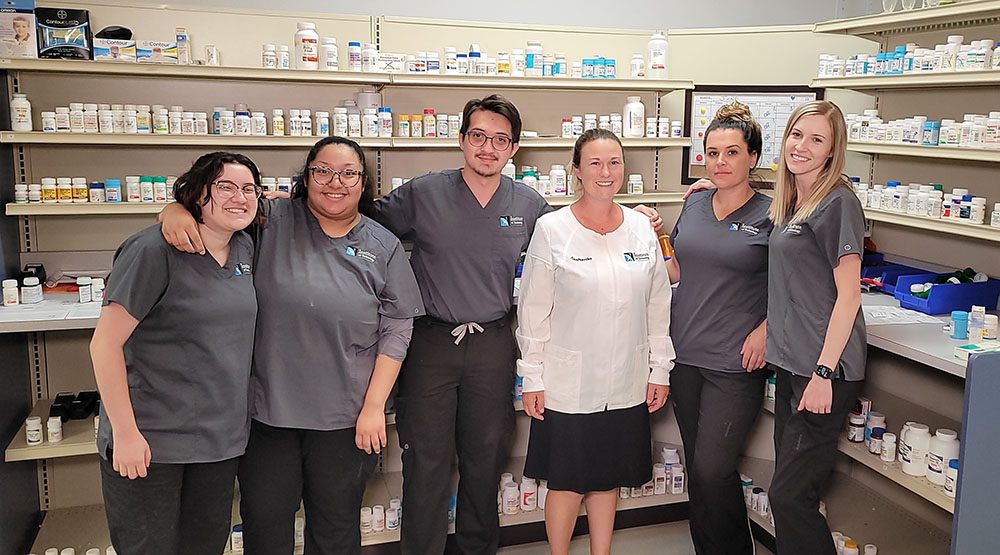 Pharmacy professor and students gathered in front of shelves of medicine smiling