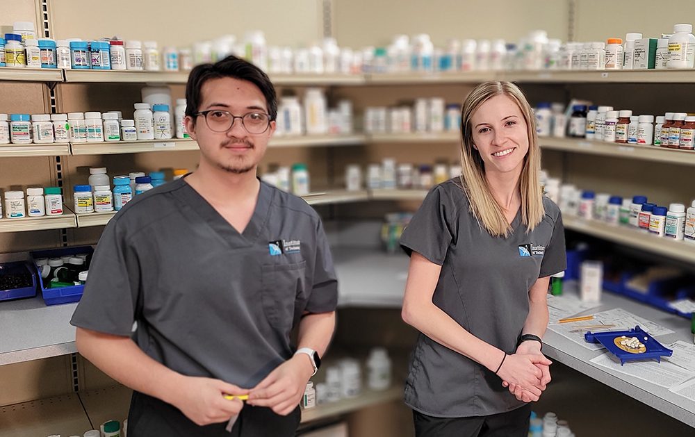 Two students in front of shelves of medicine